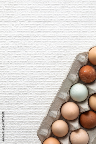Top view closeup of a fragment of carton with fresh chicken eggs on white textured background with copy space. Vertical composition