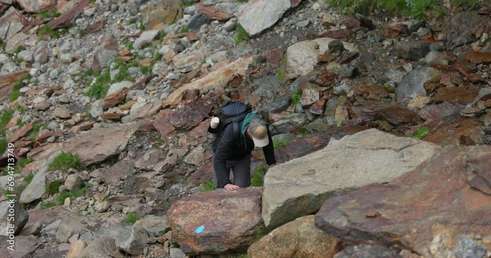 Traveler Climbing On Boulders In Valmalenco, Italy. Hiking Route To Fellaria Glacier. high angle, slowmo shot Traveler Climbing On Boulders In Valmalenco, Italy. Hiking Route To Fellaria Glacier. high angle, slowmo shot