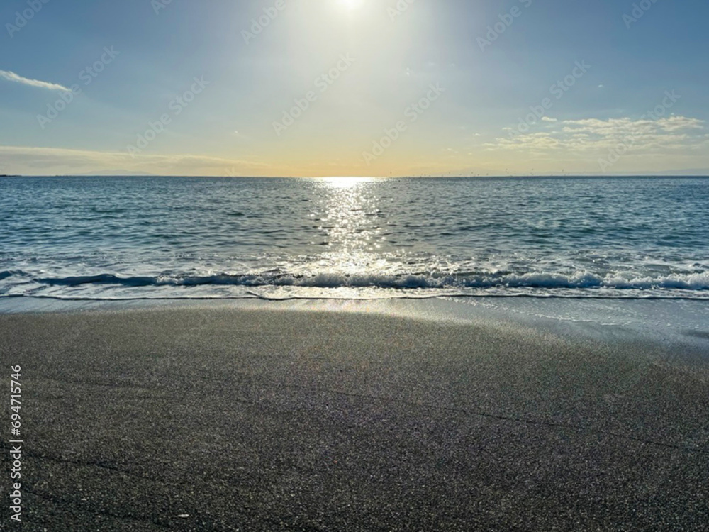 Obraz premium 大きな海に波が打ち寄せ、青い大空と太陽と夕日が混ざり合い、高台から見下ろす実写写真