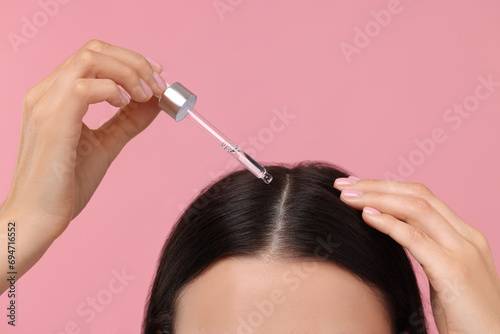 Woman applying hair serum on pink background, closeup. Cosmetic product
