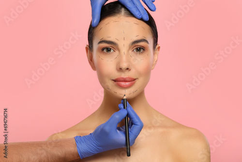 Doctor with pencil preparing patient for cosmetic surgery operation on pink background photo