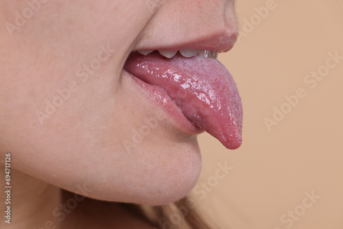 Woman showing her tongue on beige background, closeup. Space for text