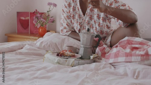Medium shot Valentines Day Breakfast in Bed beautiful dark skinned Woman enjoying Viennese Waffles Breakfast with Ice Cream and Fruits. Belgian waffles with cream on a plate with coffee on the side.