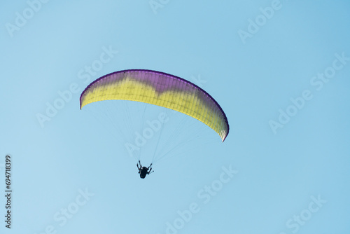 Beautiful picture of a paraglider gliding on a clear blue sky.