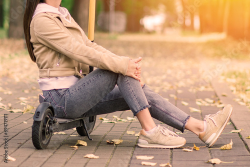 Young beautiful stylish woman riding electric scooter by autumn park, ecological transport