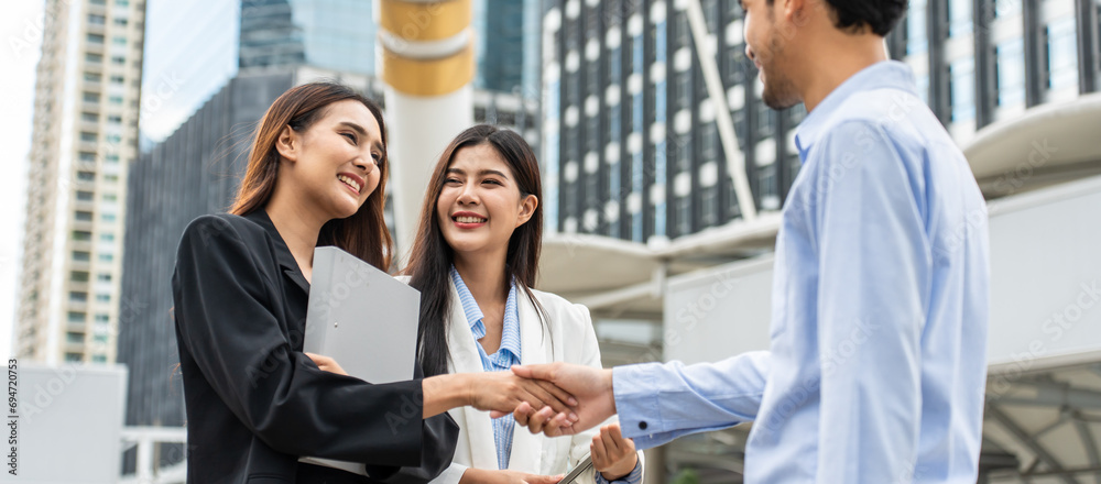 © Kawee - Asian businesswoman making handshake with businessman outdoor in city.