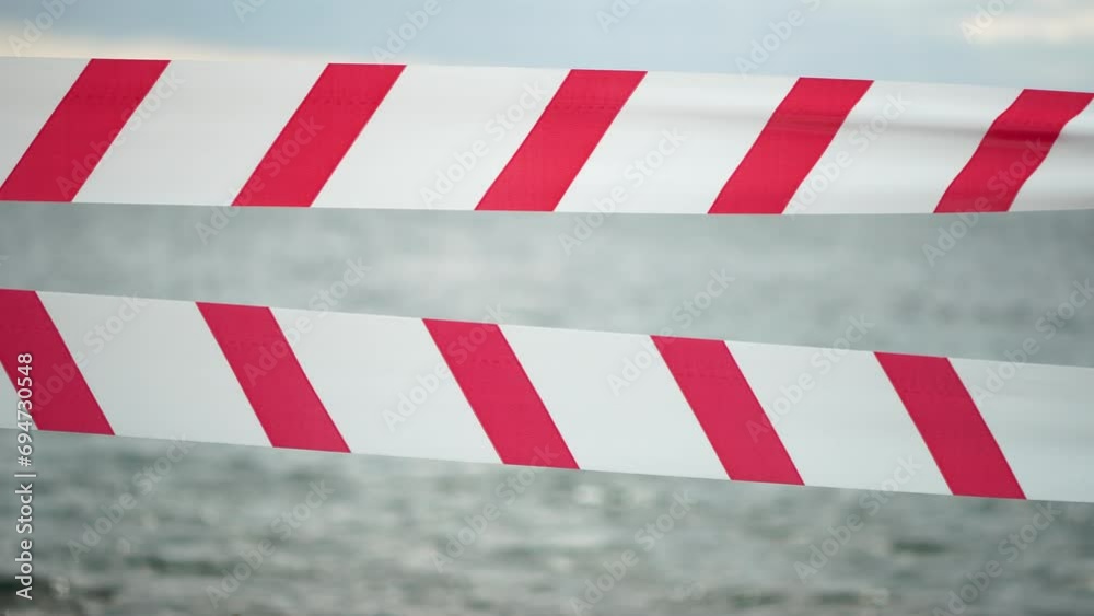 Red white warning tape barrier ribbon swinging in the wind across exotic sea beach background without people. No entry Red White caution tape. No holiday concept, delayed travel, no summer plans Red white warning tape barrier ribbon swinging in the wind across exotic sea beach background without people. No entry Red White caution tape. No holiday concept, delayed travel, no summer plans