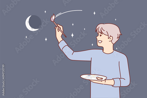 Man artist paints evening sky with moon and stars, dreaming of traveling around galaxy. Young guy artist with brush to create artistic shader and palette smiling doing creative hobby