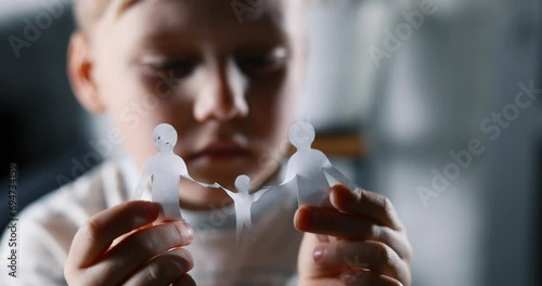 little sad boy with paper family in hands. concept of family issues, divorce, custody and child abuse photo