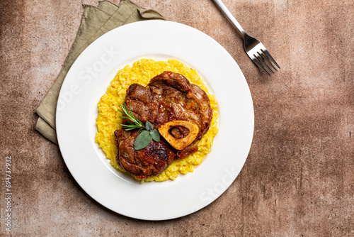 Top view of plate with Italian dish Ossobuco, braised meat served with saffron risotto alla milanese, specialty of Lombard cuisine. Brown background.