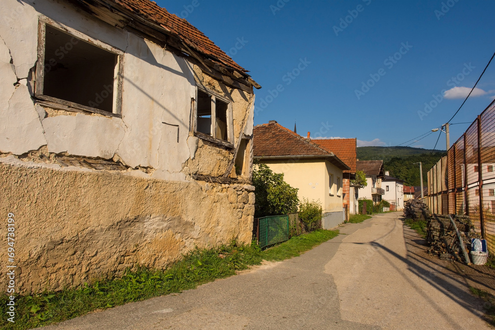 A quiet residential road in Kulen Vakuf village in the Una National Park with a derelict house on the left and sports ground on the right. Una-Sana, Federation of Bosnia and Herzegovina. Early Sept