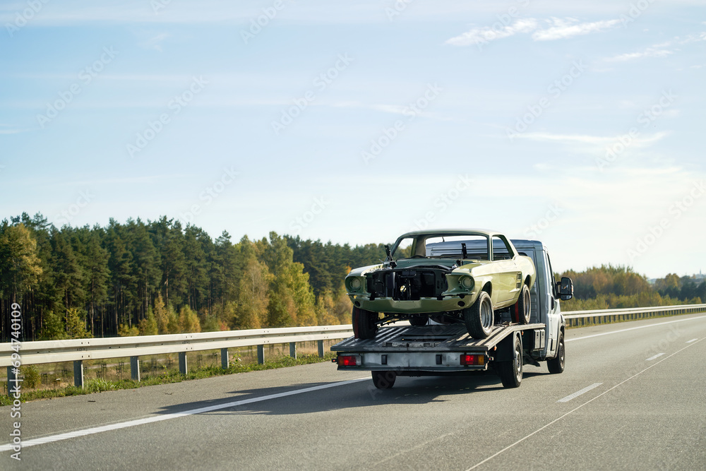 Roadside assistance transports a car with a breakdown on the road. Rollback tow truck. A tow truck delivers a failed vehicle. Roadside assistance helps a driver in trouble.