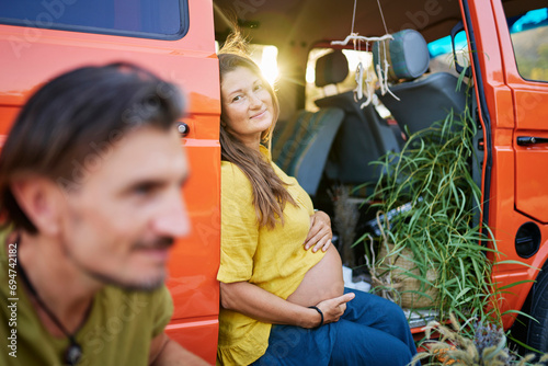 Pregnant woman sitting in caravan by male friend on vacation photo