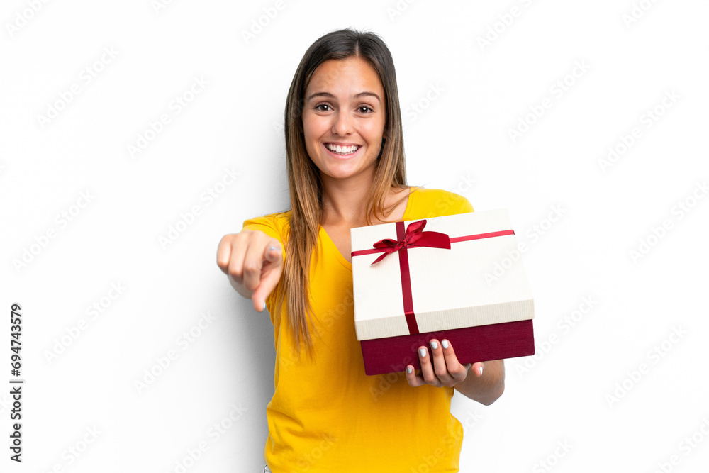 Young caucasian woman holding a gift isolated on white background points finger at you with a confident expression Young caucasian woman holding a gift isolated on white background points finger at you with a confident expression