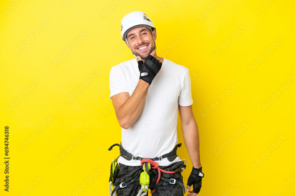 Young rock- climber man isolated on yellow background smiling Young rock- climber man isolated on yellow background smiling
