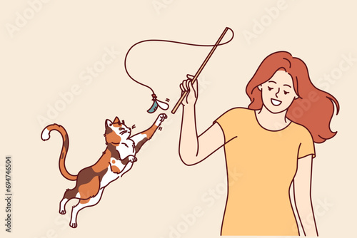 Woman plays with cat and waves bow on string, feeling pleasure thanks to presence of pet. Playful cat jumps up and stretches out paw wanting to catch kitten toy bought at pet store