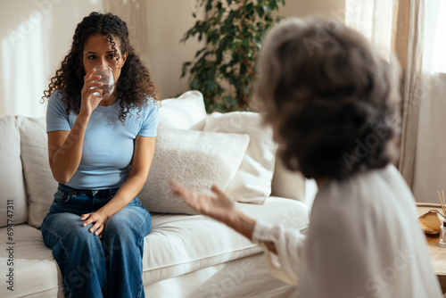 Woman drinking water and having therapy session with psychotherapist at home photo