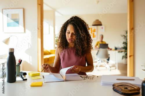 Businesswoman turning pages of note pad at desk in office photo