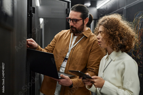 IT professionals examining servers with laptop and tablet PC in data center photo