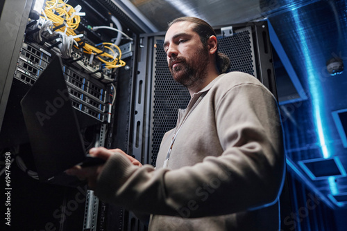 Engineer working on laptop near server room equipment photo