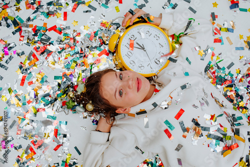 Smiling girl lying near confetti with clock on floor photo