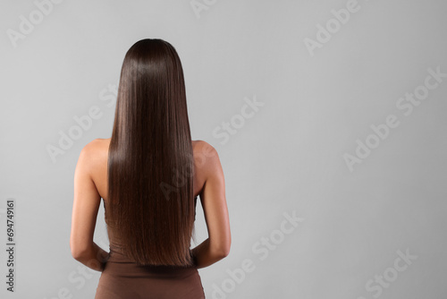 Hair styling. Woman with straight long hair on grey background, back view and space for text