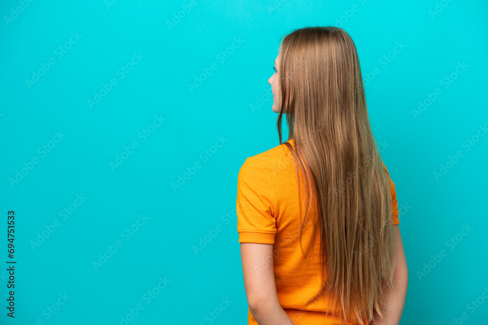 Young Russian woman isolated on blue background in back position and looking back Young Russian woman isolated on blue background in back position and looking back