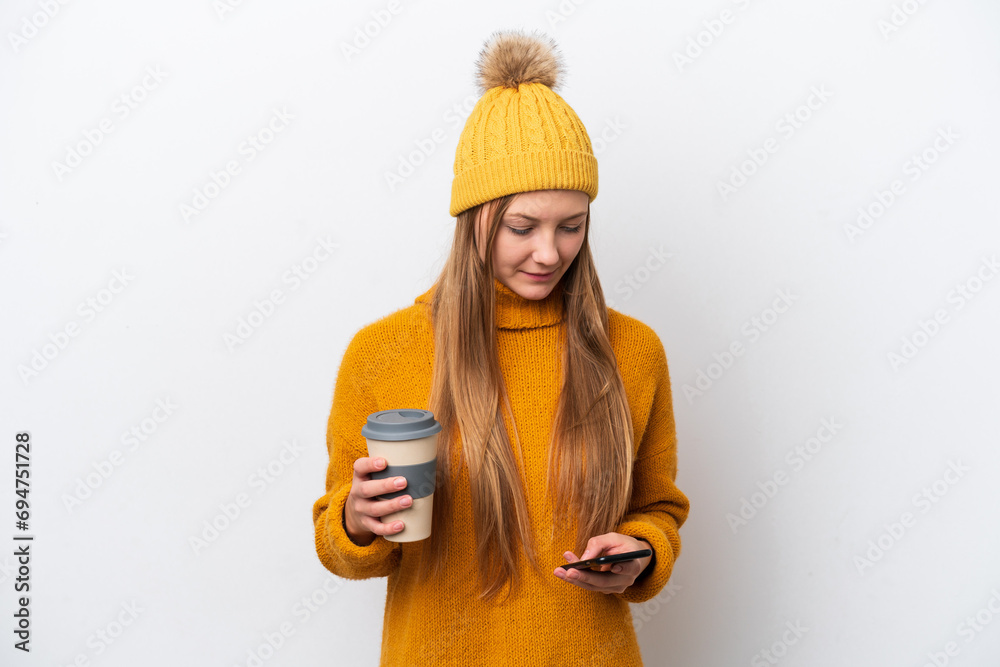 Young caucasian woman wearing winter jacket isolated on white background holding coffee to take away and a mobile Young caucasian woman wearing winter jacket isolated on white background holding coffee to take away and a mobile