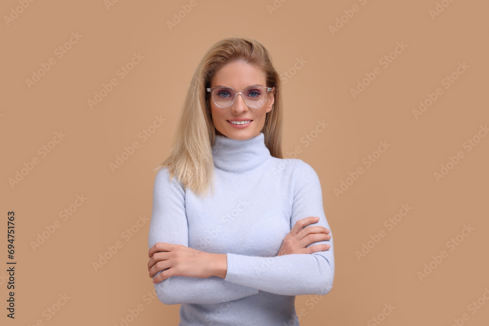 Fototapeta premium Portrait of smiling middle aged woman in glasses with crossed arms on beige background