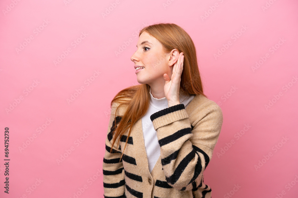 Fototapeta premium Young redhead woman isolated on pink background listening to something by putting hand on the ear