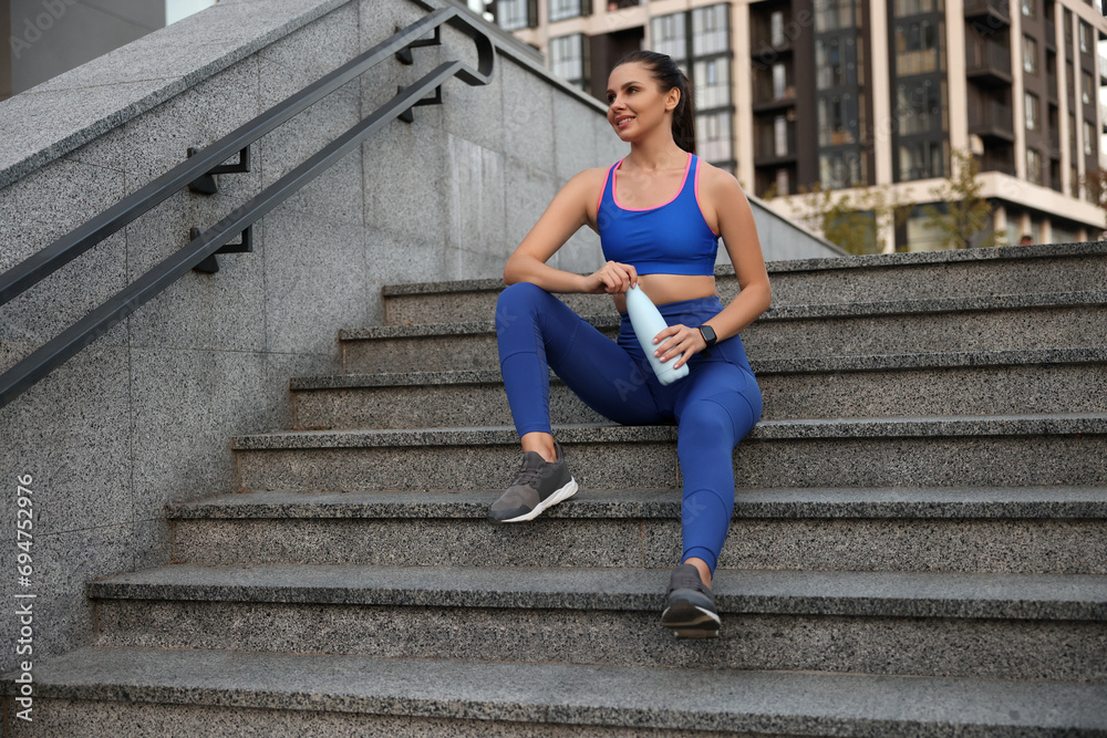 Obraz premium Beautiful woman in stylish sportswear with bottle of drink on stairs outdoors