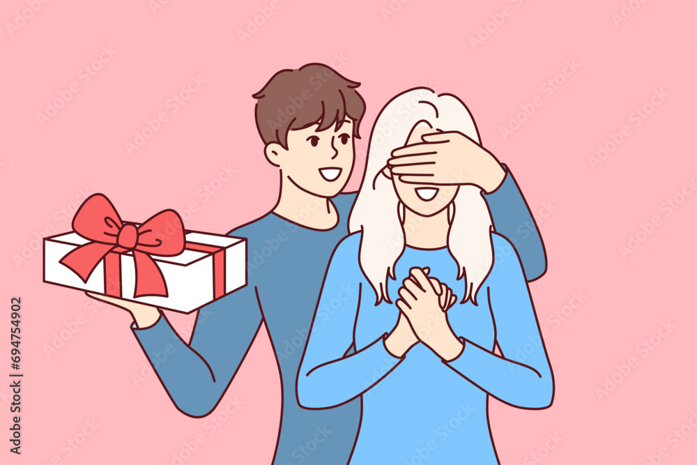 Groom surprises girlfriend standing with gift box and covering girl eyes with hand. Boyfriend in love congratulates happy bride on birthday and Christmas or valentine day on february 14th. Groom surprises girlfriend standing with gift box and covering girl eyes with hand. Boyfriend in love congratulates happy bride on birthday and Christmas or valentine day on february 14th.