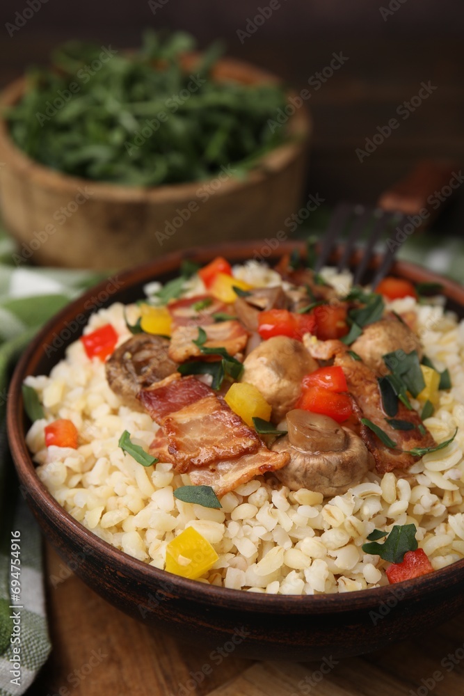 Cooked bulgur with vegetables, fried bacon and mushrooms in bowl on wooden table, closeup Cooked bulgur with vegetables, fried bacon and mushrooms in bowl on wooden table, closeup