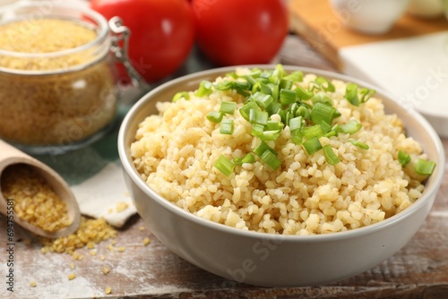 Delicious bulgur with green onion on wooden table, closeup