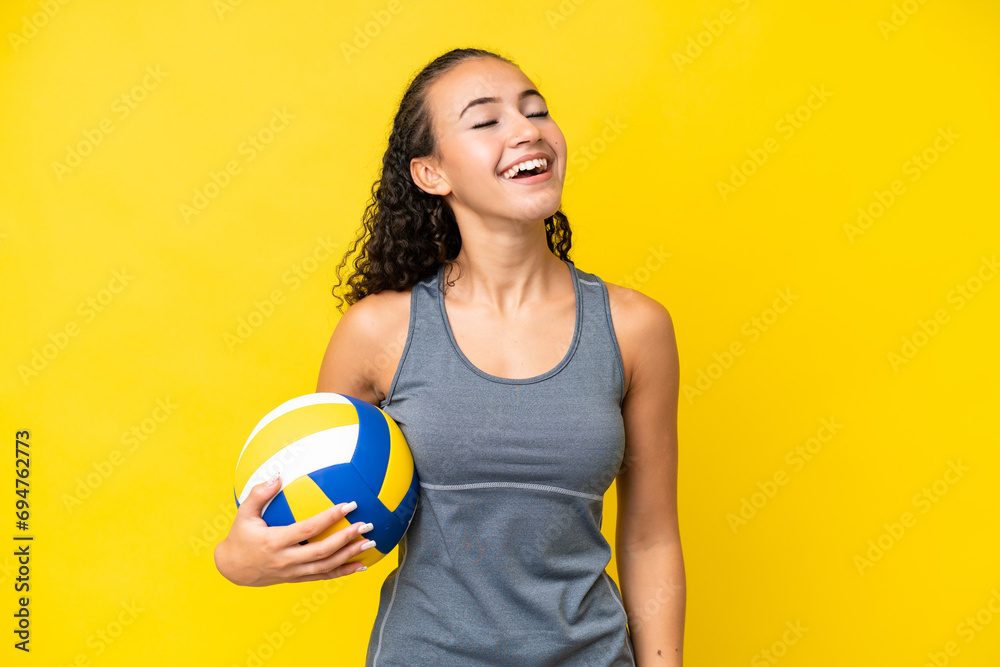 Young woman playing volleyball isolated on yellow background laughing