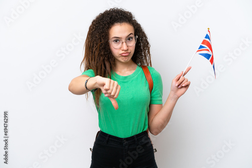 Young Arab woman holding an United Kingdom flag isolated on white background showing thumb down with negative expression
