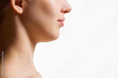 Cropped side view image of female face, neck isolated against white studio background. Reduction of double chin. photo
