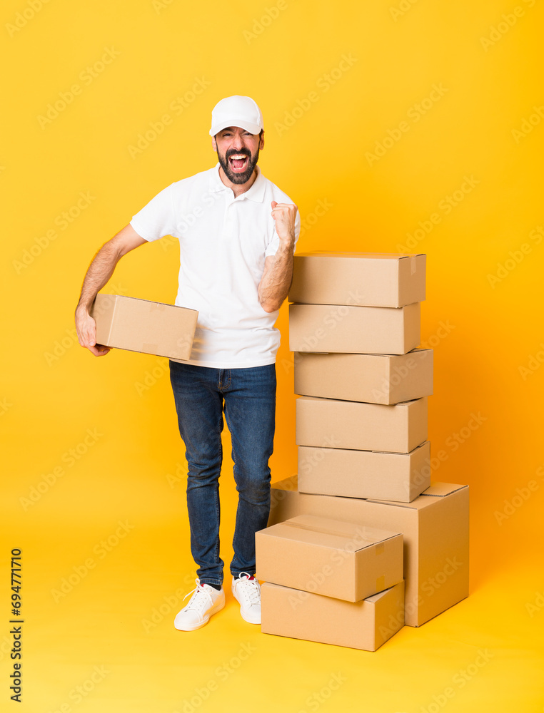Full-length shot of delivery man among boxes over isolated yellow background frustrated by a bad situation Full-length shot of delivery man among boxes over isolated yellow background frustrated by a bad situation