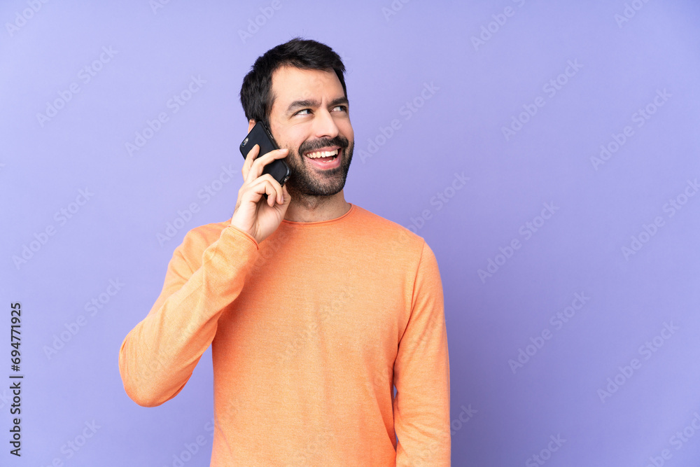 Caucasian handsome man over isolated purple background keeping a conversation with the mobile phone