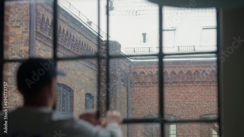 Person gazes thoughtfully through a snow-dappled window, historic brick building backdrop. photo