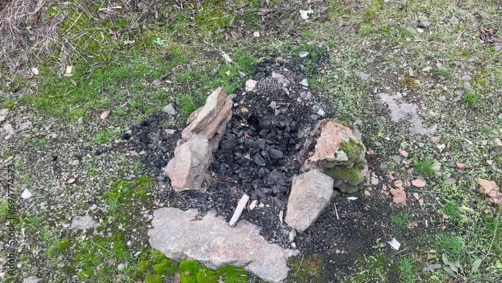 an extinguished fire with dark coals lined with bricks on a green lawn