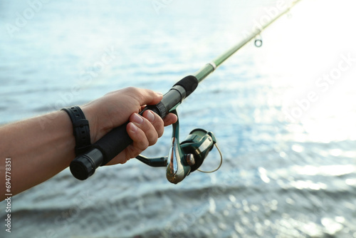 Fisherman with rod fishing at riverside, closeup. Space for text