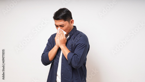 Young Adult Asian man cover his nose and mouth with tissue when sneezing on white background. studio shot