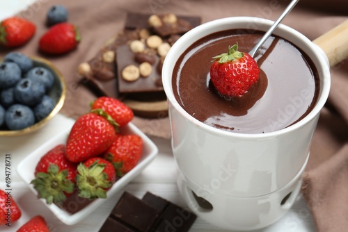 Dipping fresh strawberry in fondue pot with melted chocolate at white table  closeup