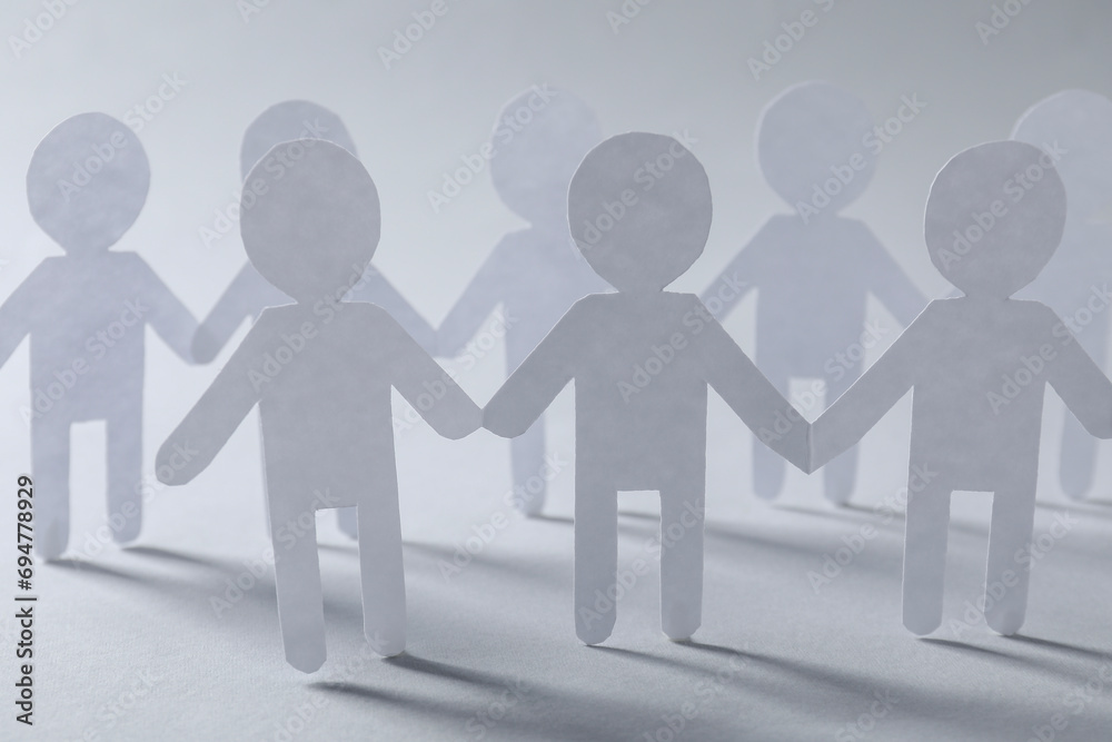 Teamwork concept. Paper figures of people holding hands on light grey background, closeup Teamwork concept. Paper figures of people holding hands on light grey background, closeup