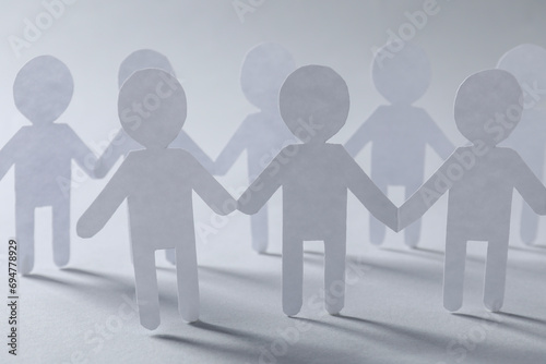 Teamwork concept. Paper figures of people holding hands on light grey background, closeup