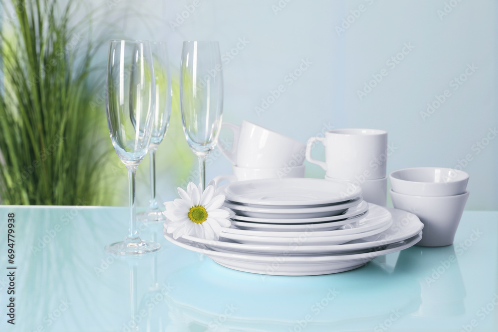 Set of clean dishware and flower on light blue table Set of clean dishware and flower on light blue table