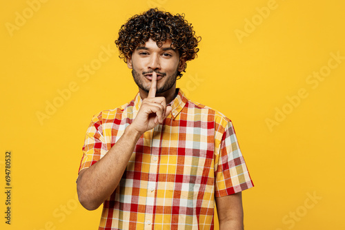 Young secret Indian man he wearing shirt casual clothes say hush be quiet with finger on lips shhh gesture looking camera isolated on plain yellow color background studio portrait. Lifestyle concept.