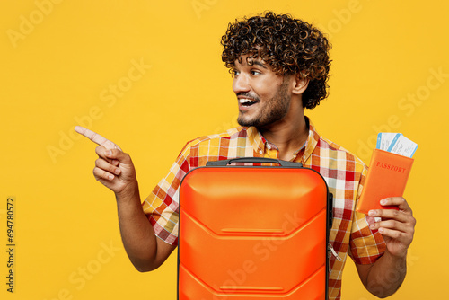 Traveler Indian man wear casual clothes hold bag passport ticket point aside isolated on plain yellow background Tourist travel abroad in free spare time rest getaway. Air flight trip journey concept