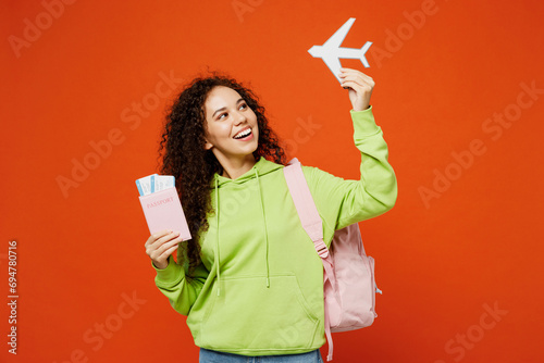 Traveler young teen girl student wear casual clothes hold passport ticket plane isolated on plain orange background. Tourist travel abroad in free time getaway. High school university college concept. photo